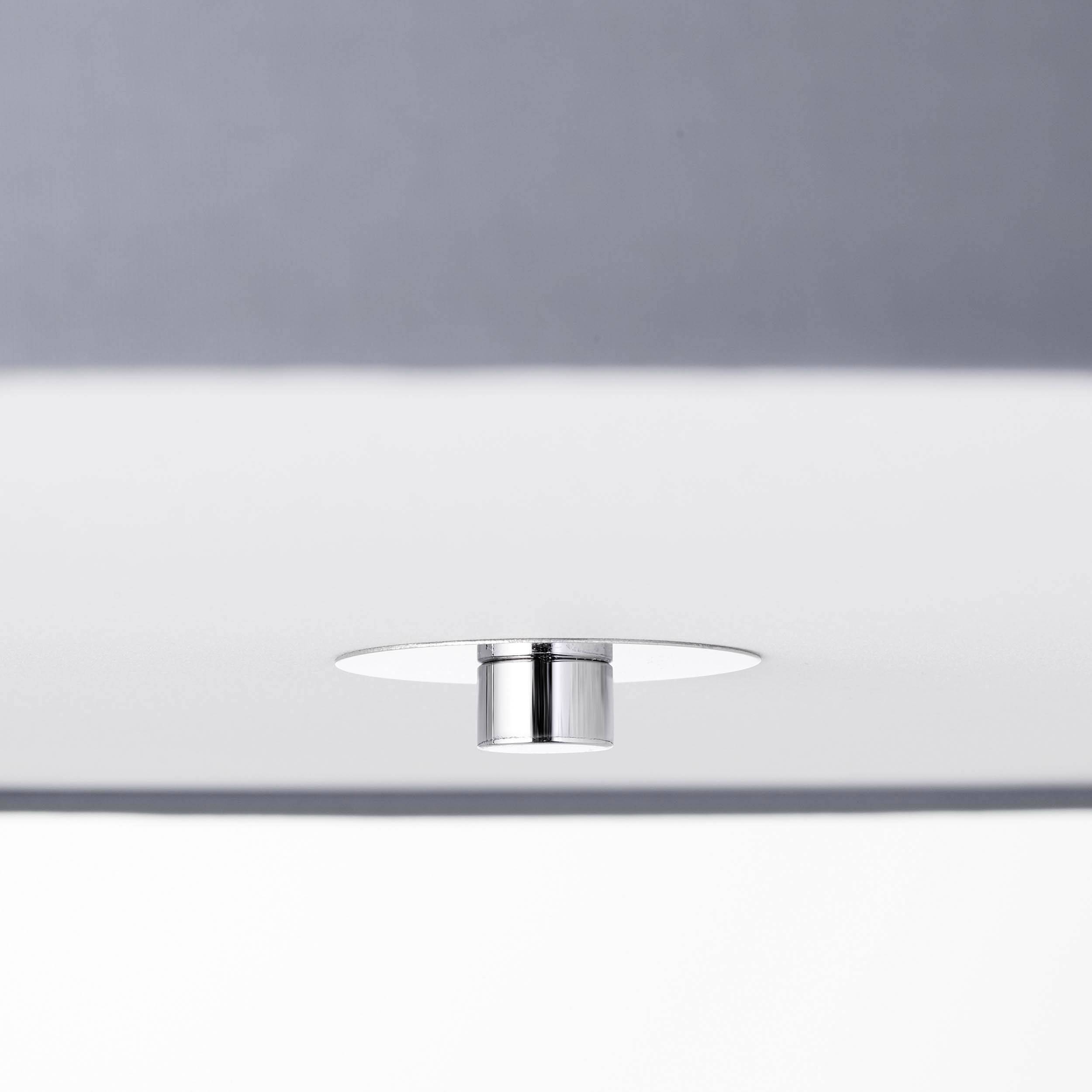 Un luminaire de plafond minimaliste, rond, avec un cadre en métal argenté sur un fond gris.