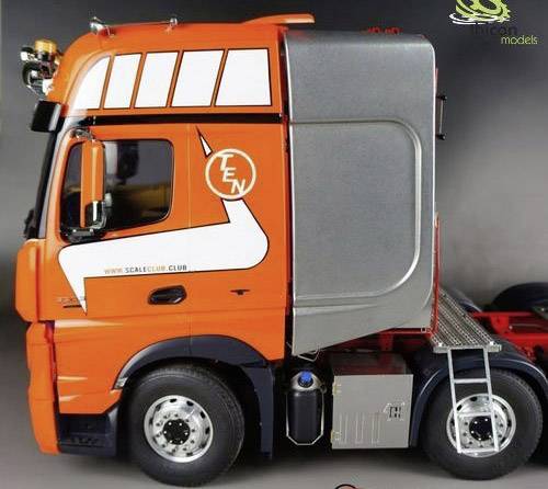 Un camion orange avec des éléments graphiques blancs sur le côté est stationné sur un fond gris. Le camion a une cabine argentée.