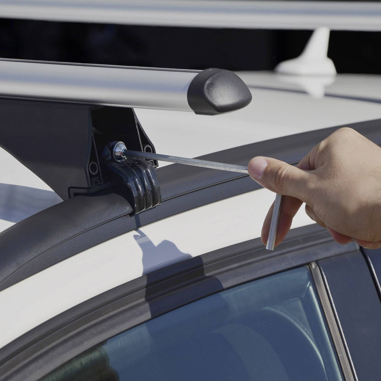 Une main retire une vis d'une barre de toit d'une voiture à l'aide d'un outil plat.