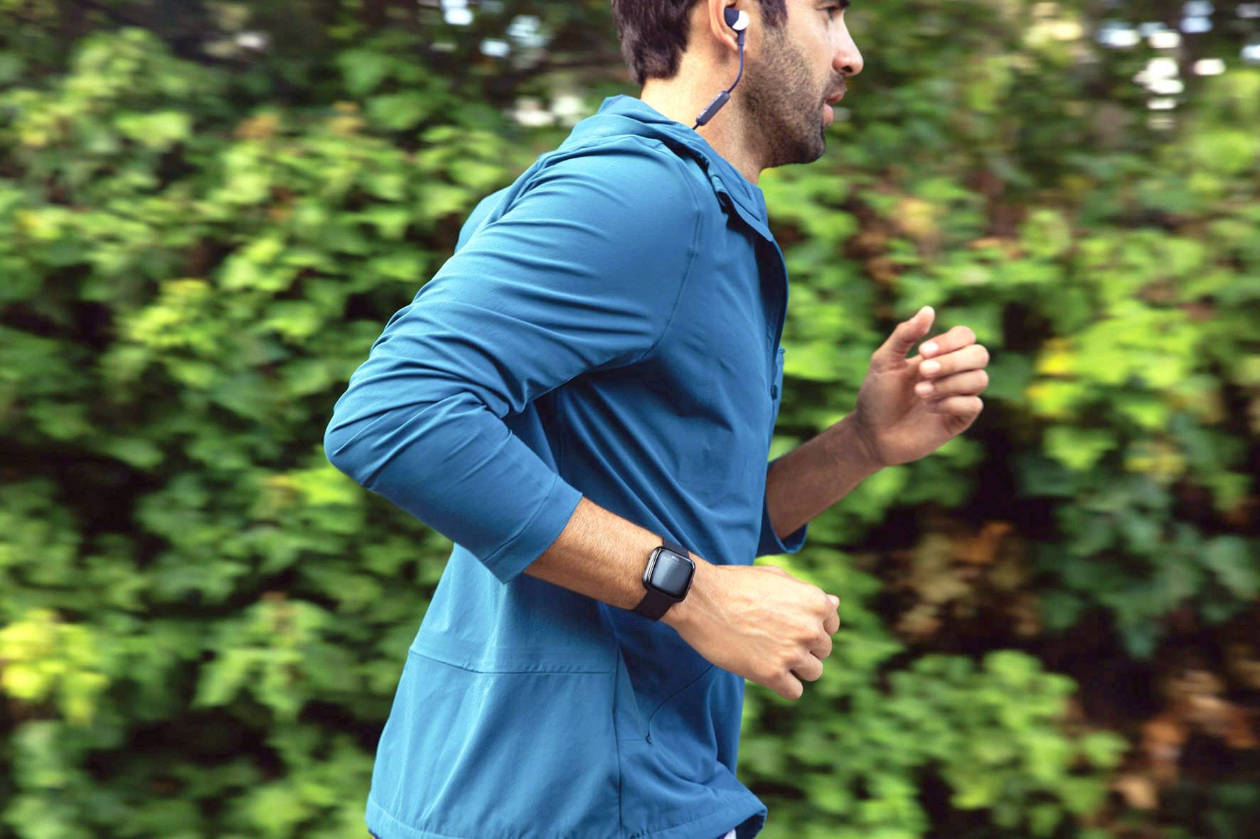 Un homme court avec des écouteurs bleus et une montre connectée dans la nature.