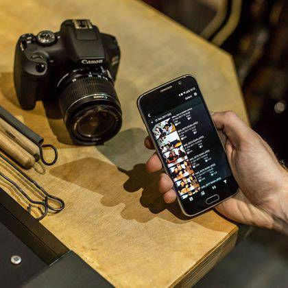 Un appareil photo est posé sur une table à côté d'un smartphone tenu dans une main. Sur l'écran du téléphone, des photos sont visibles.
