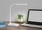 Bureau moderne avec lampe LED blanche, ordinateur portable ouvert et plante dans un vase en verre, idéal pour un travail ou un apprentissage productif.