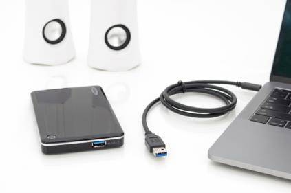 Disque dur externe avec câble USB, à côté d'un ordinateur portable et d'enceintes sur une table blanche.