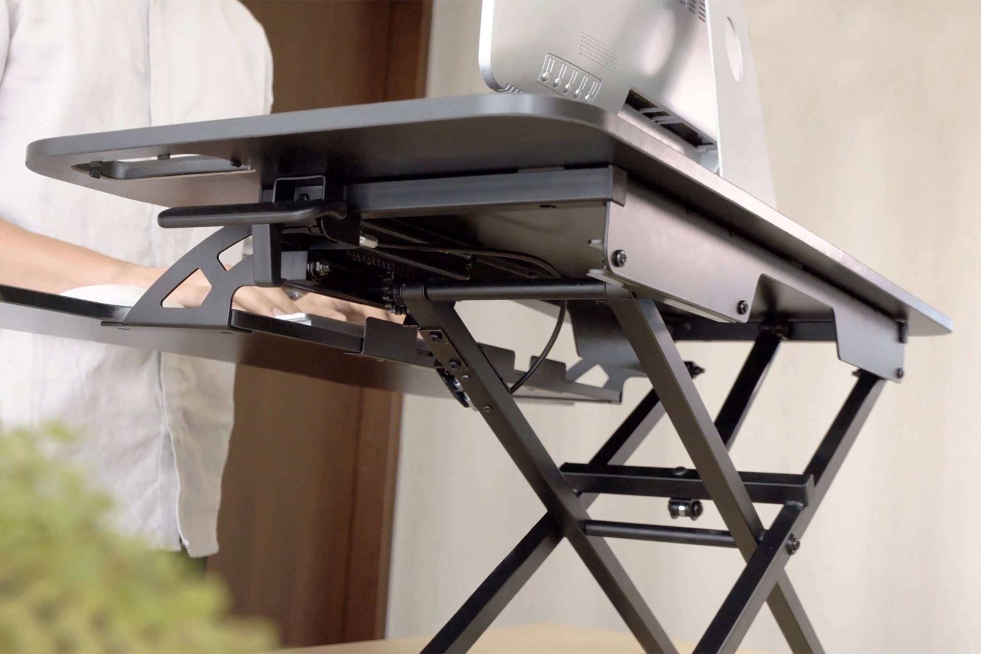 Un bureau réglable en hauteur avec un ordinateur portable, une personne debout qui tape ; illustre une solution ergonomique de poste de travail.