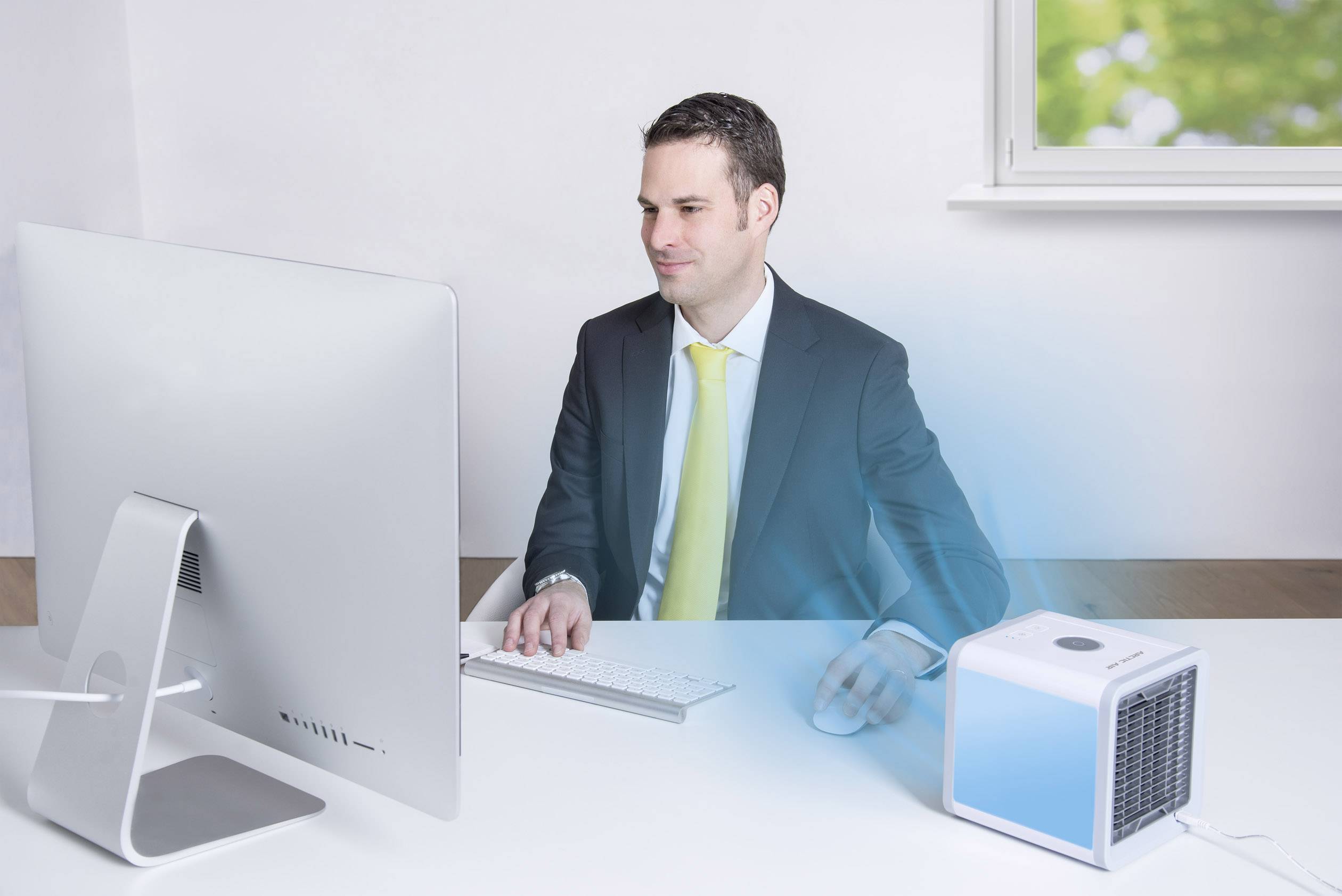 Un homme en costume travaille sur ordinateur, tandis qu'un petit climatiseur à éclairage bleu est posé sur son bureau.