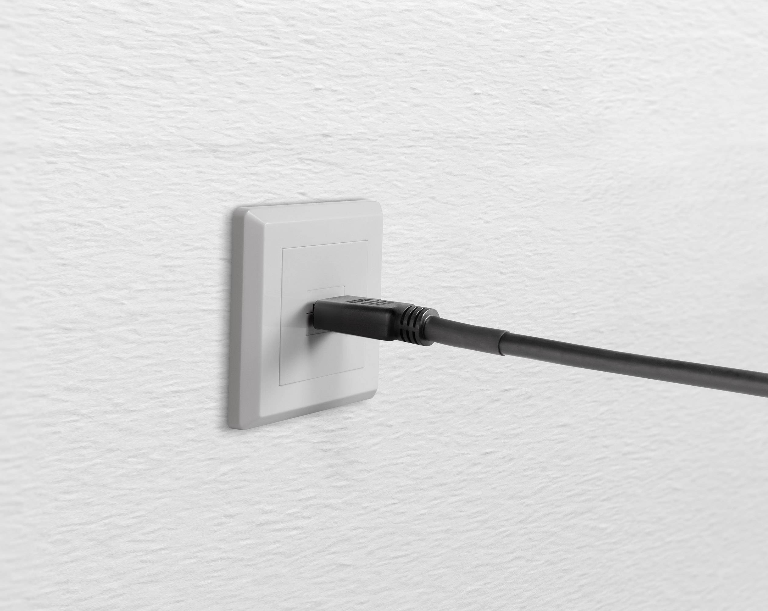 Un câble noir est branché dans une prise réseau blanche montée sur un mur blanc structuré.