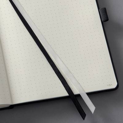 Un carnet ouvert aux pages pointillées, avec deux signets en noir et blanc, est posé sur une surface grise.