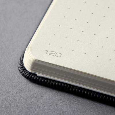 Coin d'un carnet avec des pages pointillées et le chiffre '120'. Les bords de page montrent une pile ; reliure à spirale noire visible.