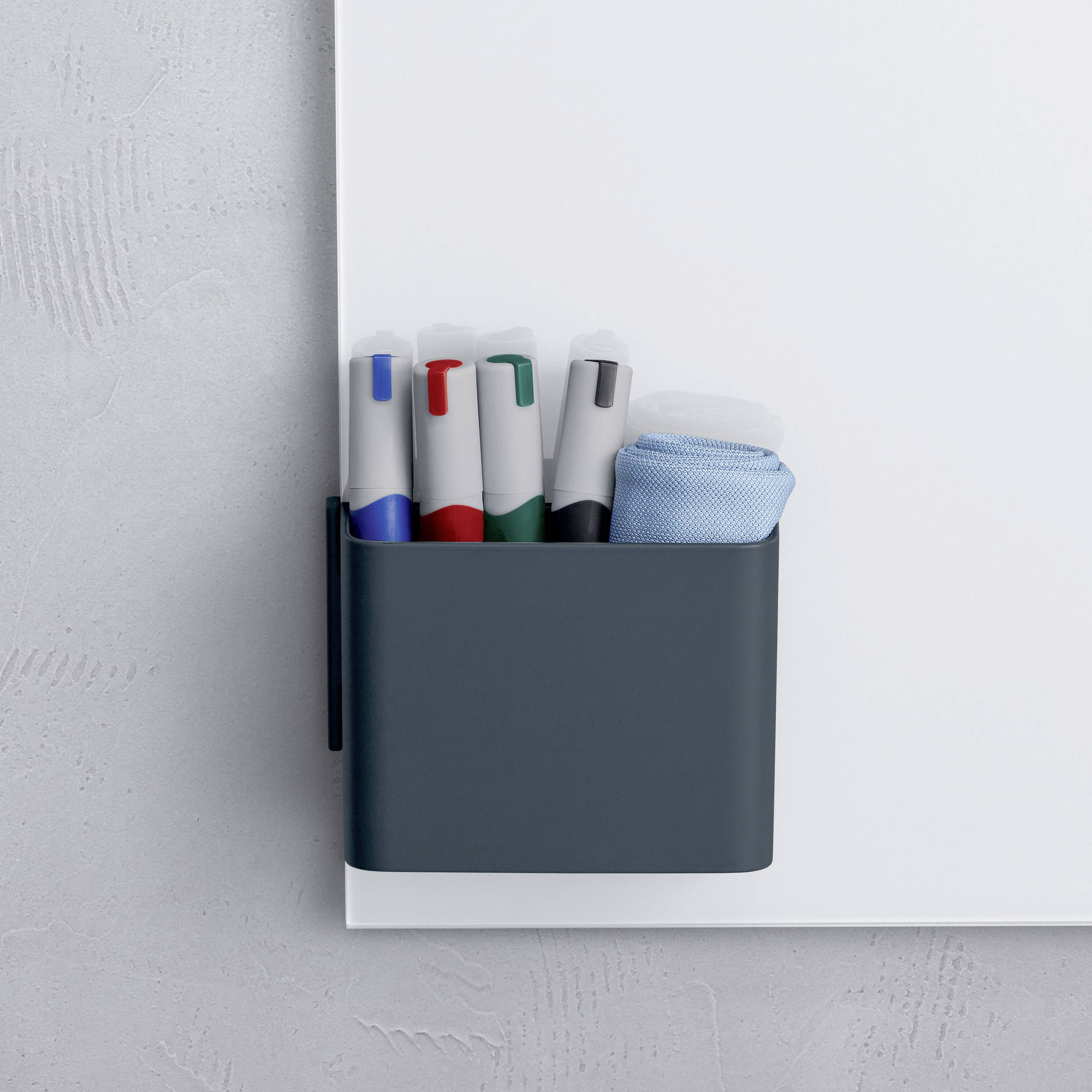 Tableau blanc avec support pour quatre marqueurs de couleurs différentes et une éponge effaceur, fixé à un mur gris.