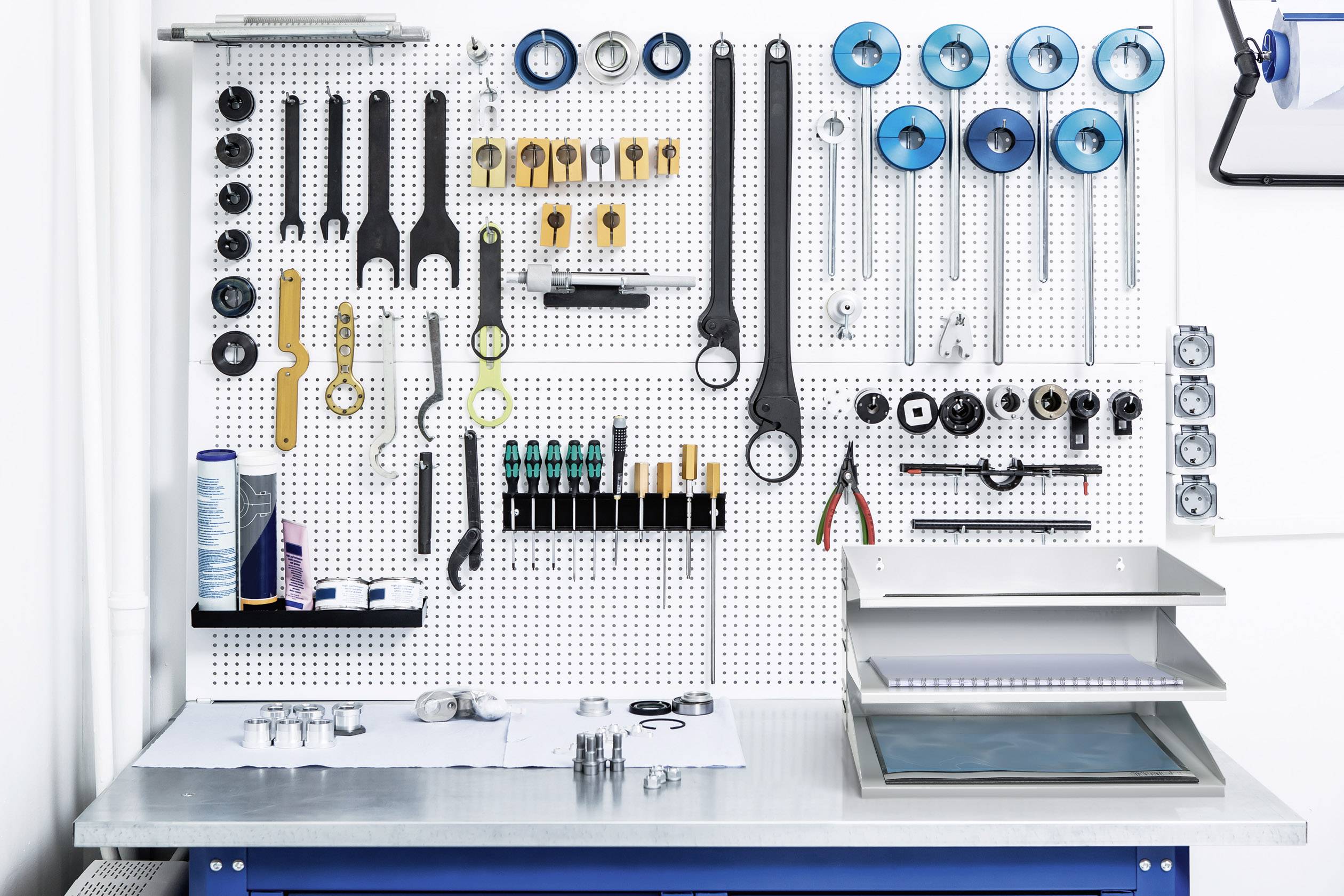 Établi avec panneau à outils : clés, pinces, tournevis, vis et autres outils soigneusement rangés.