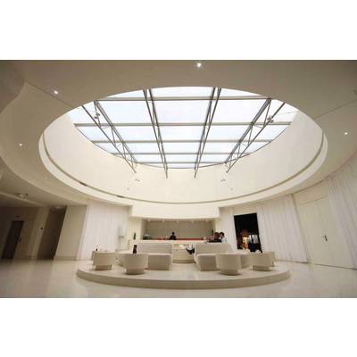 Grand espace lumineux avec un plafond circulaire en verre, en dessous se trouvent des meubles blancs modernes et quelques personnes ; une bar est visible en arrière-plan.