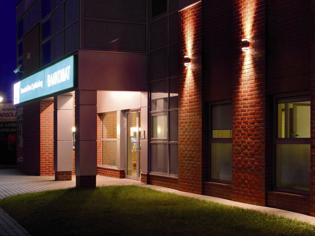 Un bâtiment éclairé la nuit avec une façade en verre et en brique. Un panneau lumineux au-dessus de l'entrée.