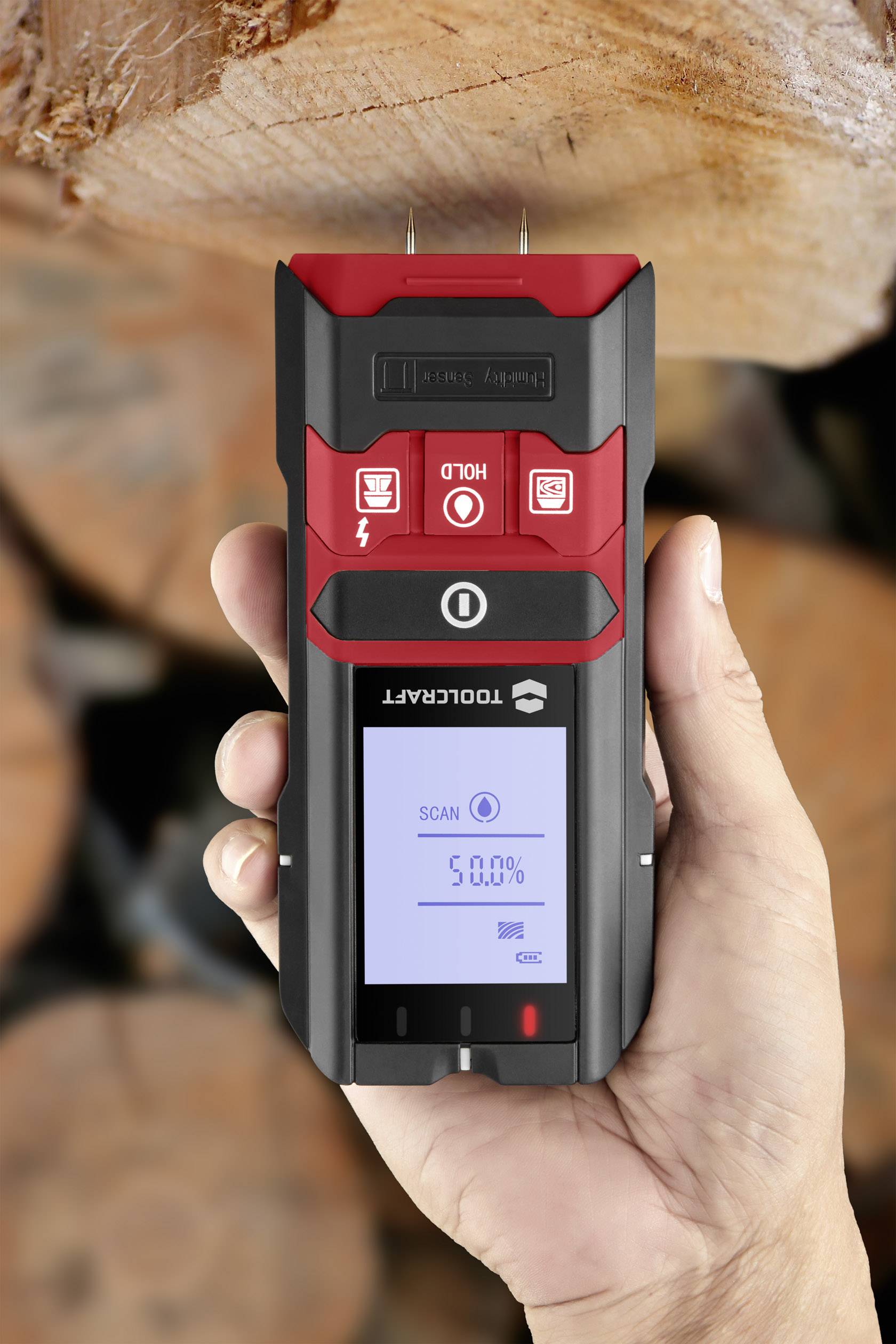 Un appareil portable pour mesurer l'humidité du bois affiche '50,0%' sur un écran. Arrière-plan : surfaces de bois floues.