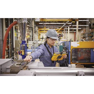 Un homme portant un casque de protection utilise une machine dans une usine. Il tient une tablette à la main et se trouve entouré d'équipements techniques.
