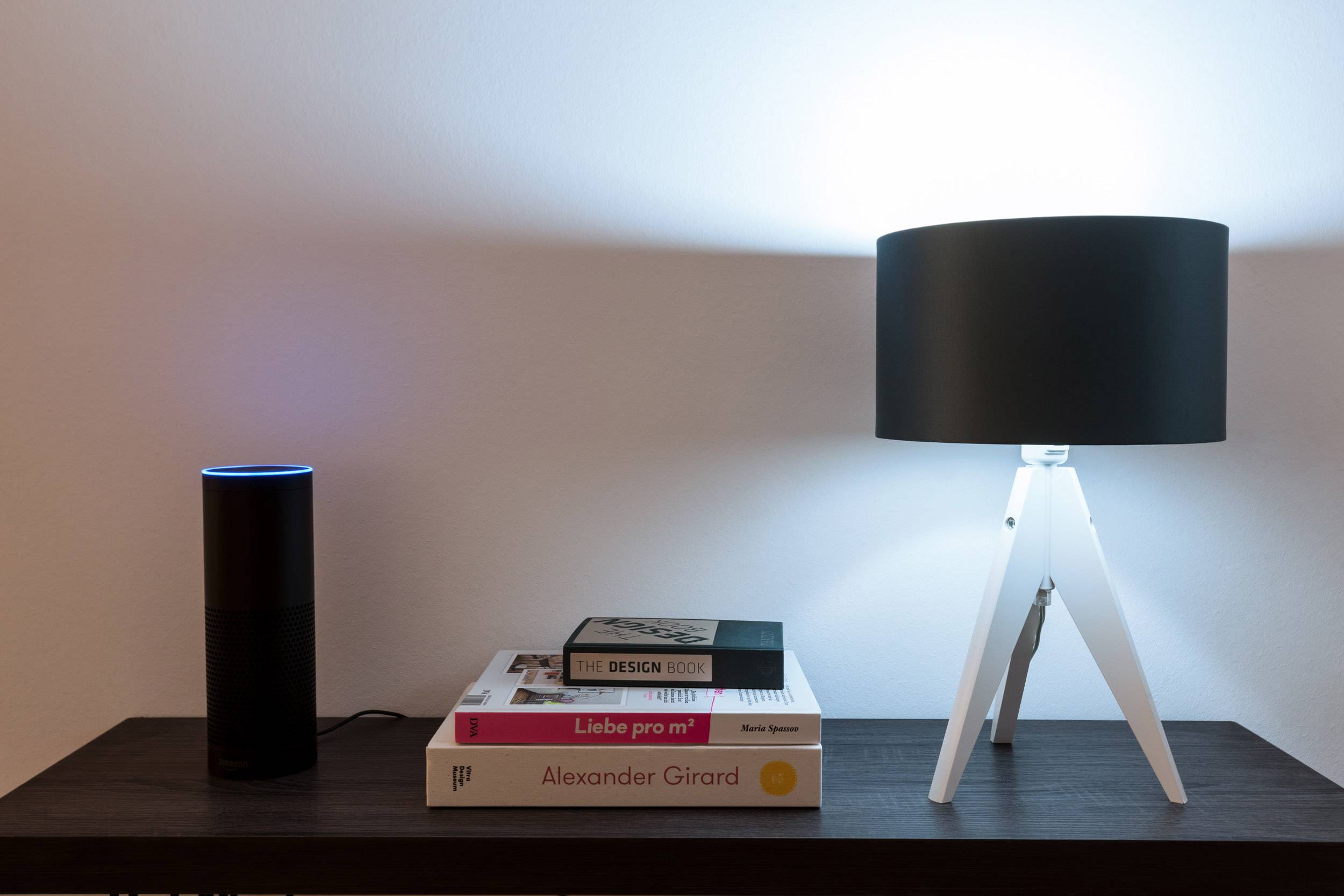 Un haut-parleur noir avec une lumière bleue est posé à côté d'une lampe allumée sur une table recouverte de livres.