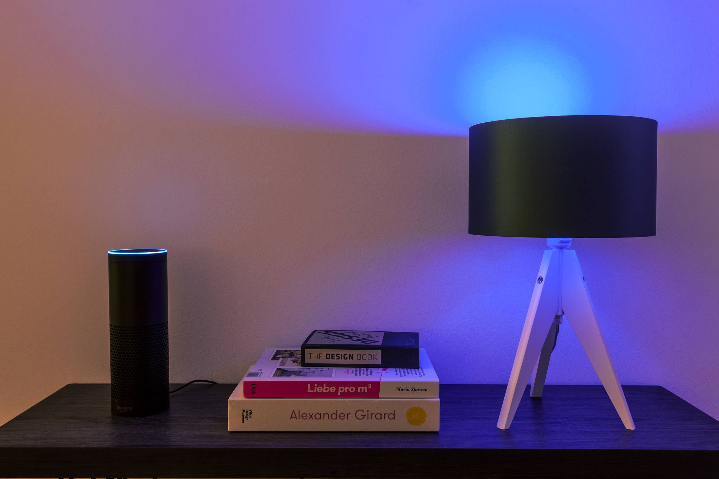 Une étagère avec un assistant vocal, une lampe à lumière bleue et des livres ; illustrant la technologie domestique intelligente et un aménagement moderne.