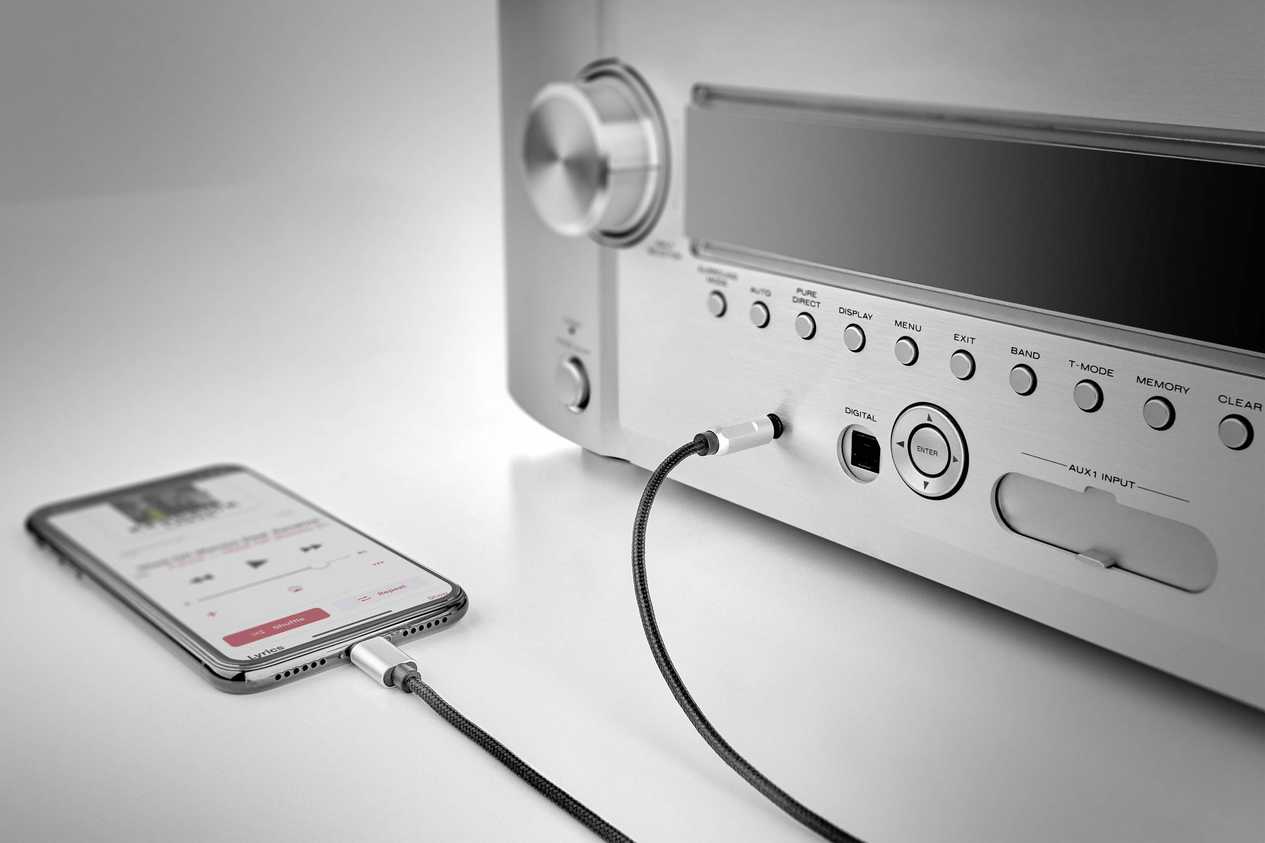 Un smartphone est connecté à un amplificateur via un câble, affichant un lecteur de musique sur son écran.