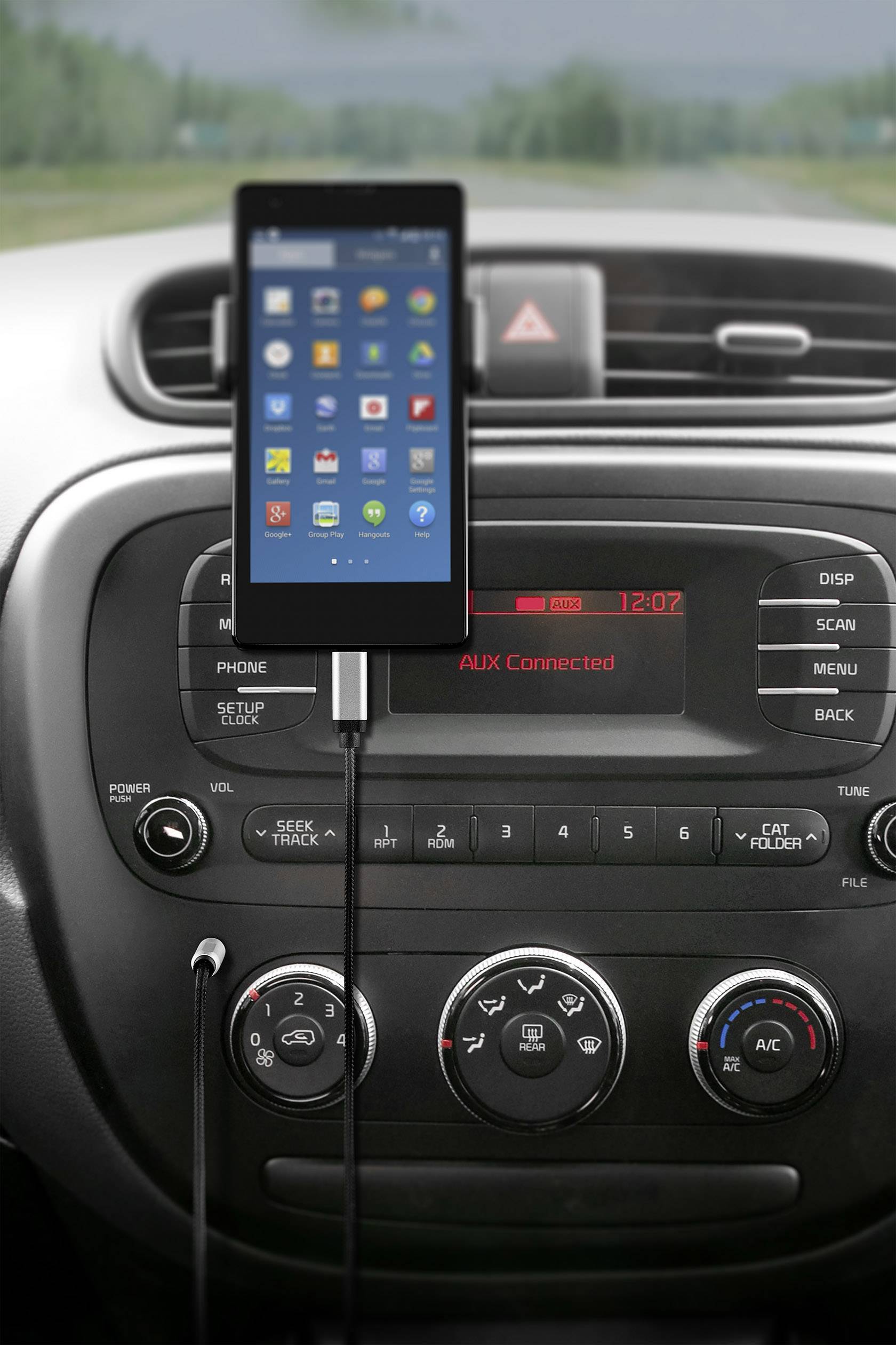 Smartphone dans un support fixé à la console centrale d'une voiture. Des icônes d'applications sont visibles sur l'écran. La radio affiche « AUX Connecté ».