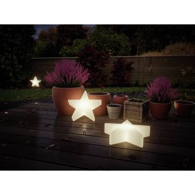 Un jardin au crépuscule avec des lampes étoilées lumineuses et des pots contenant des plantes mauves sur une terrasse en bois.