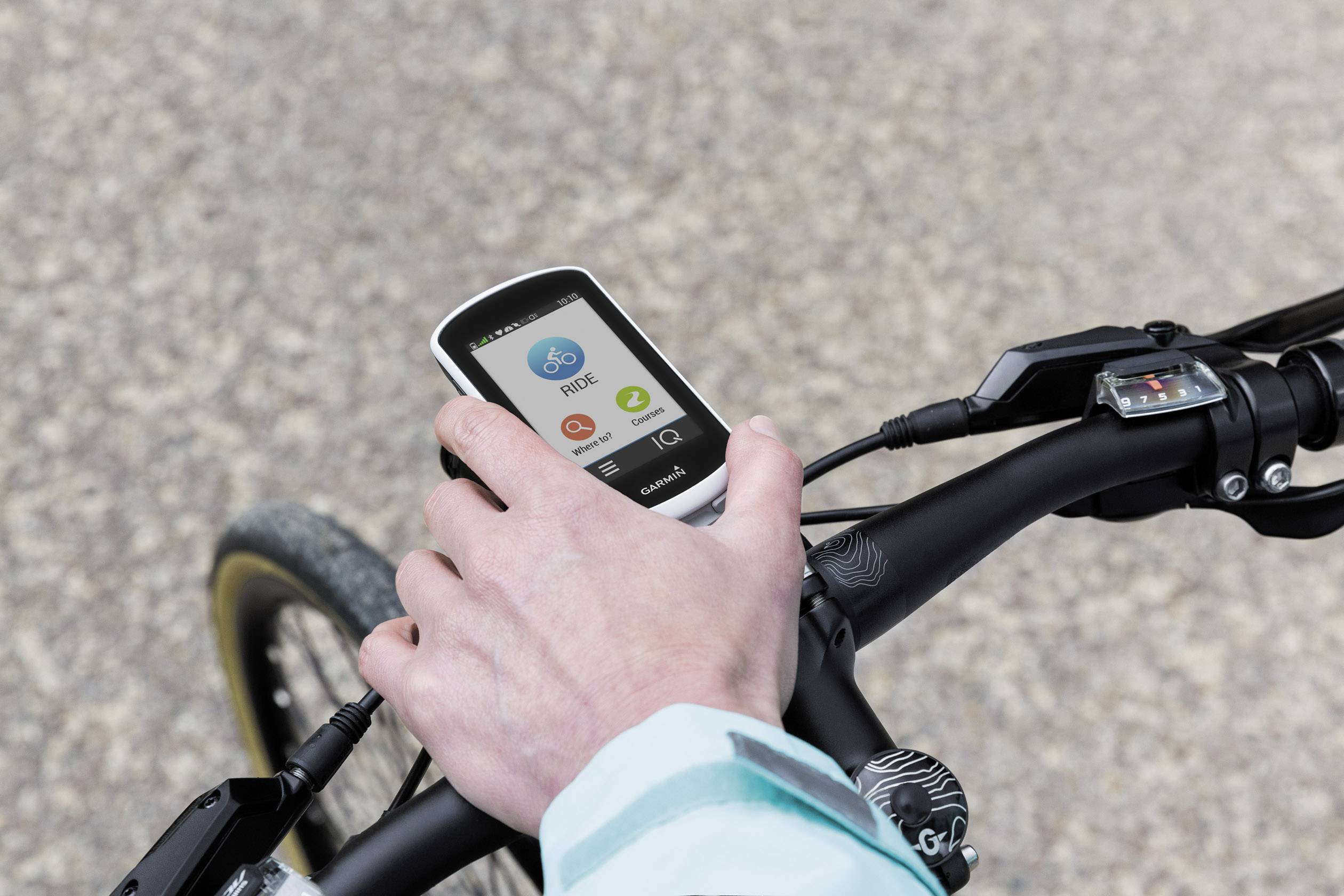 Une main tient un guidon de vélo équipé d'un appareil GPS. L'écran affiche 'Ride' et montre des informations sur le trajet cycliste.