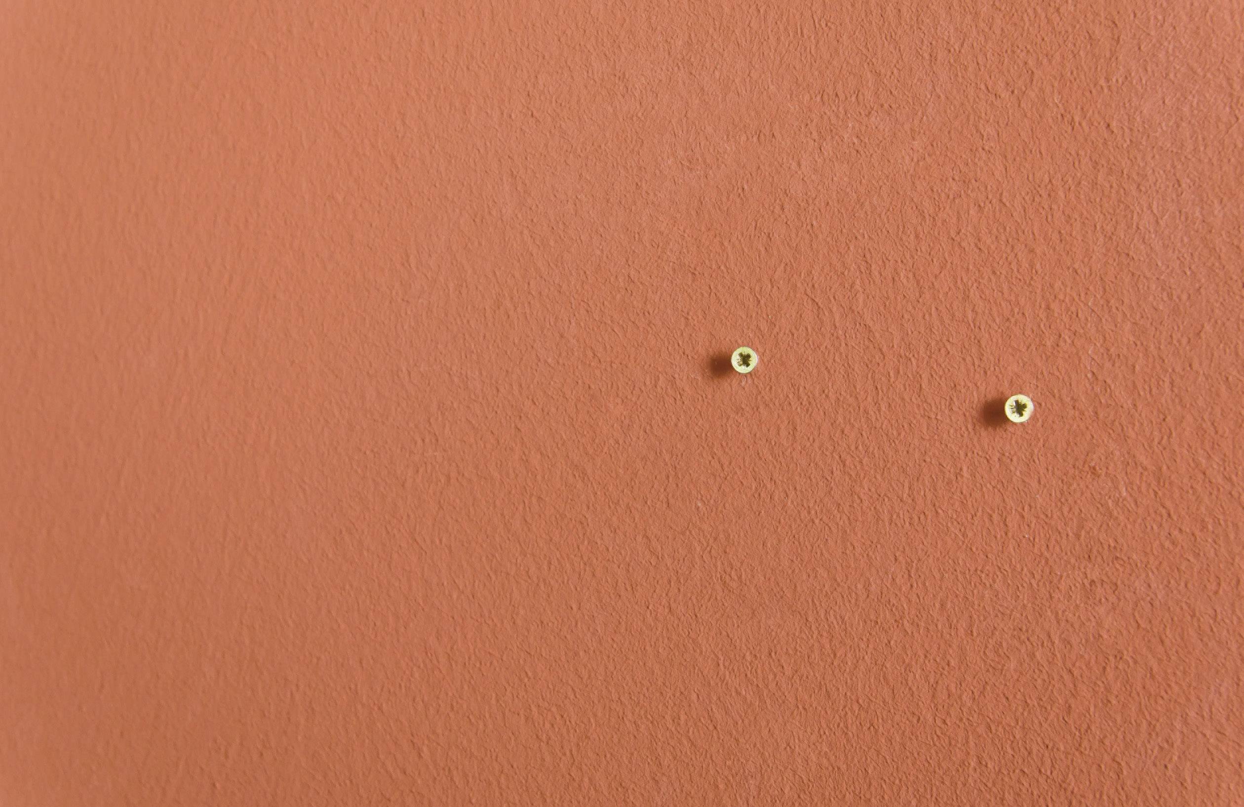 Un mur orange avec deux petites vis dorées placées au centre, très proches l'une de l'autre.
