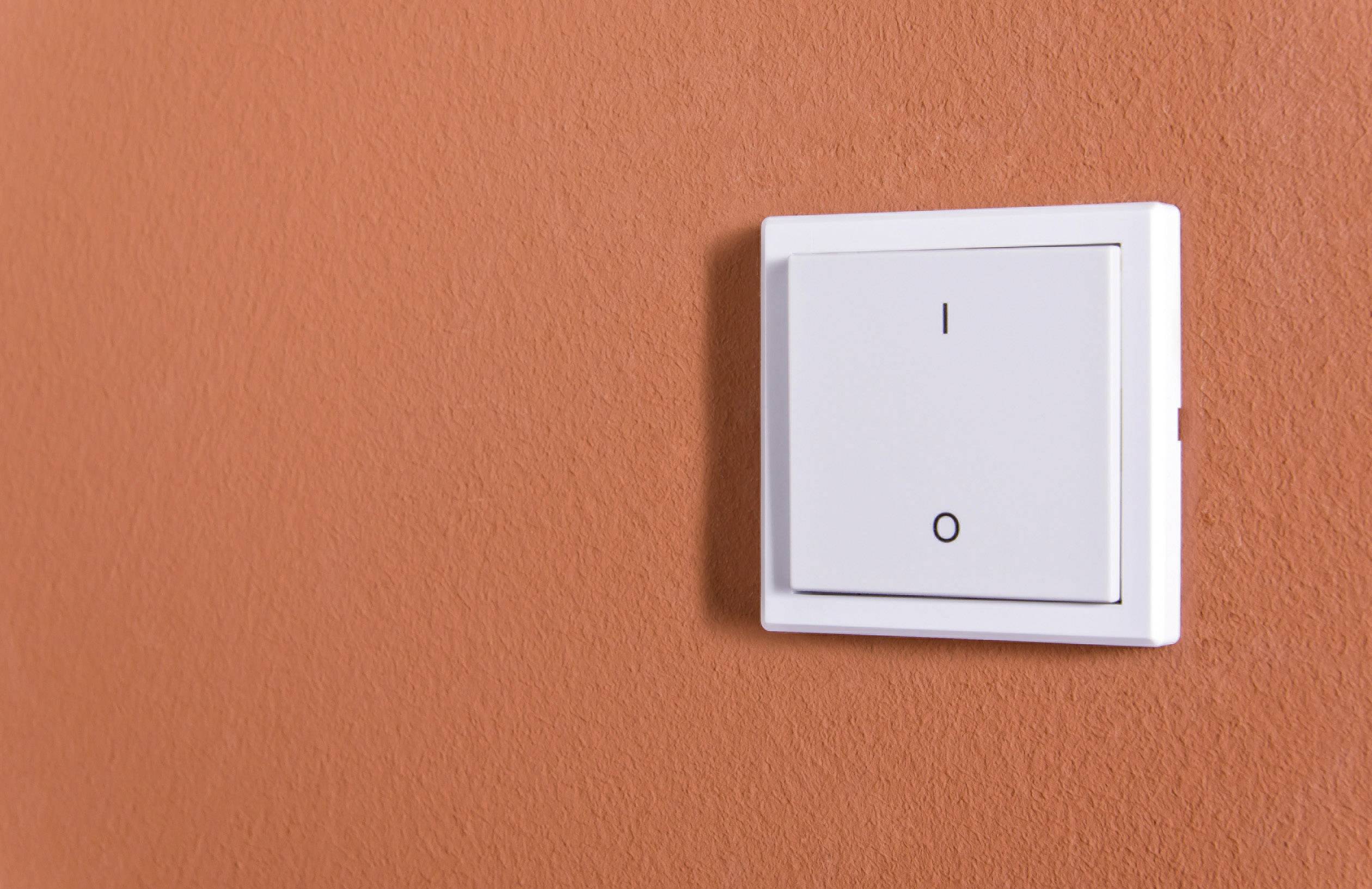 Un interrupteur blanc sur un mur orange, en position 'Éteint'.