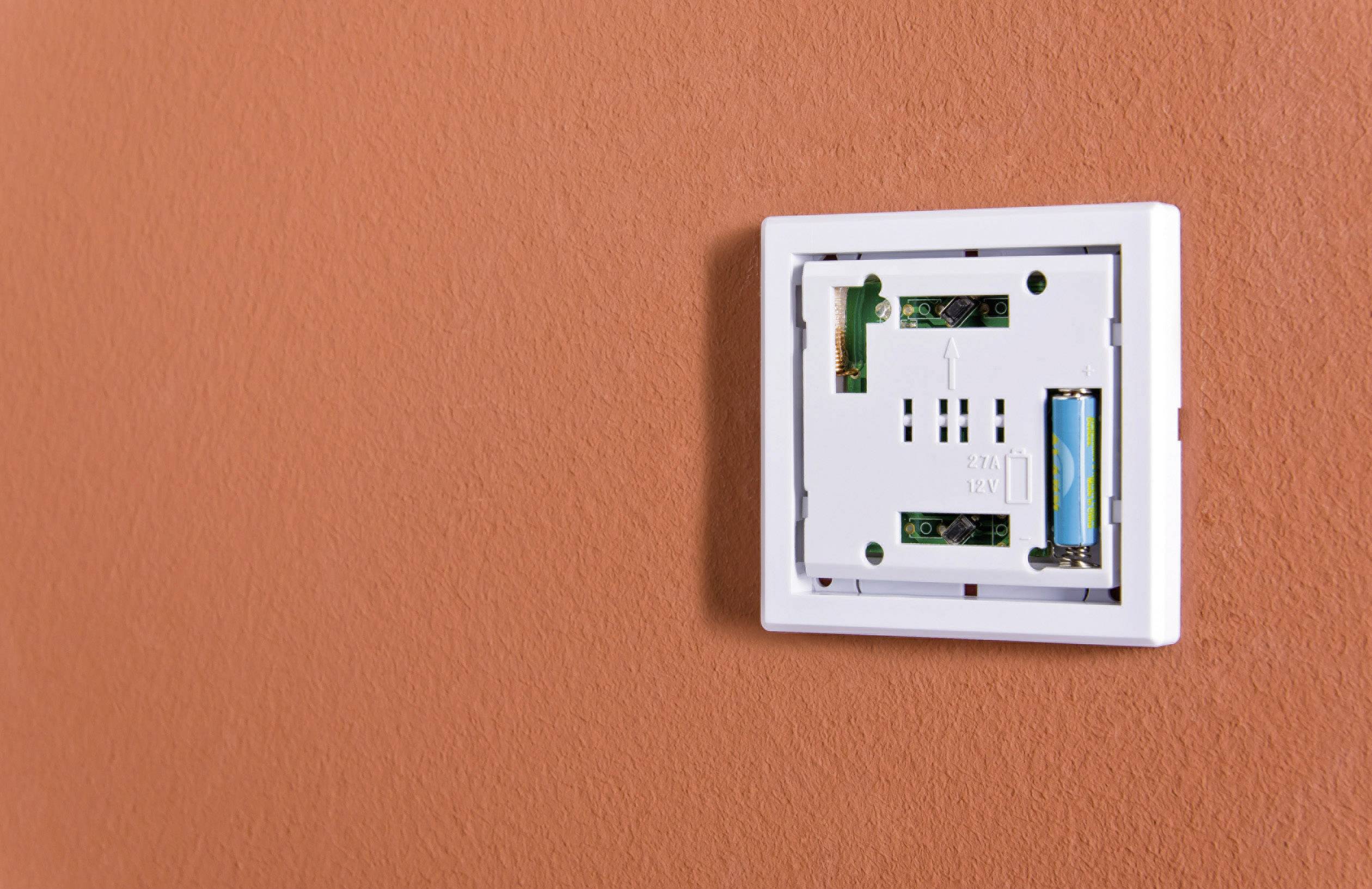 Prise électrique vide sans couvercle sur un mur orange, révélant le câblage électrique et le compartiment de la batterie.