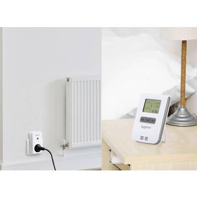 Un thermostat de radiateur et une prise murale sont représentés à côté d'un thermostat numérique. Un lit est visible en arrière-plan.