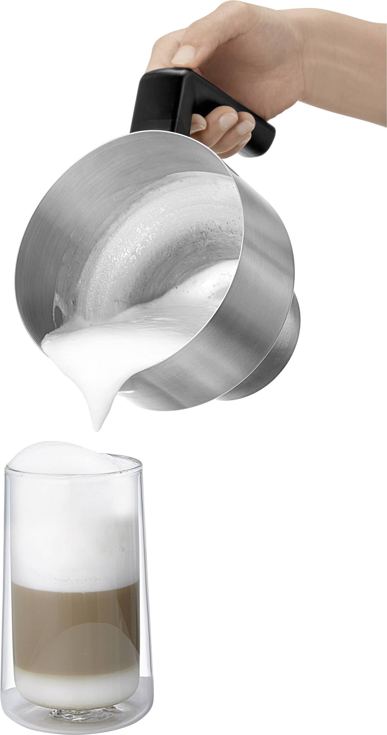 Une main tient une cruche en métal et verse du lait mousseux dans un verre de café pour préparer un latte macchiato.