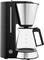 Une machine à café filtre noire avec une carafe en verre et des accents argentés. Des graduations sur la carafe indiquent le niveau de remplissage.