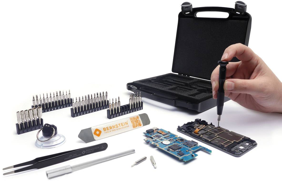 Une main utilise un tournevis pour travailler sur un circuit électronique ouvert. Les outils et les embouts sont soigneusement disposés à côté.