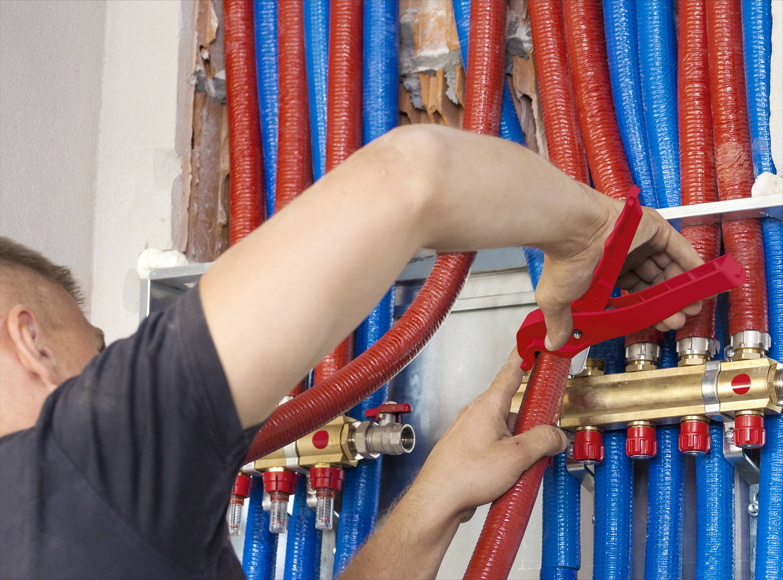 Un artisan installe des tuyaux rouges et bleus dans un système de chauffage. L'accent est mis sur l'ajustement précis des conduites.