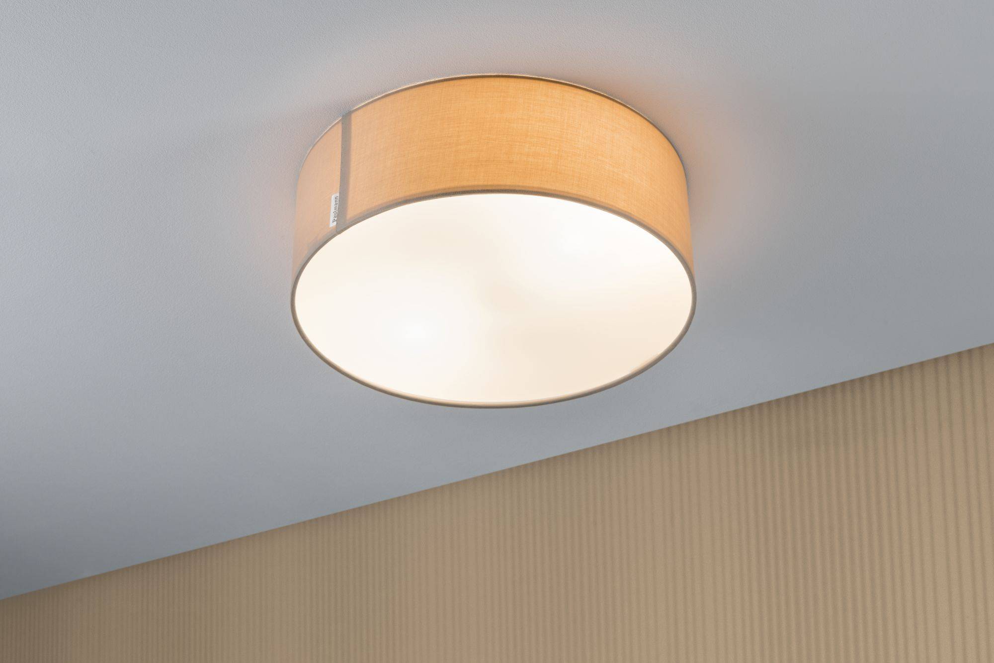 Luminaire plafonnier rond en bois clair, monté sur un plafond blanc, diffusant une lumière chaleureuse dans la pièce.