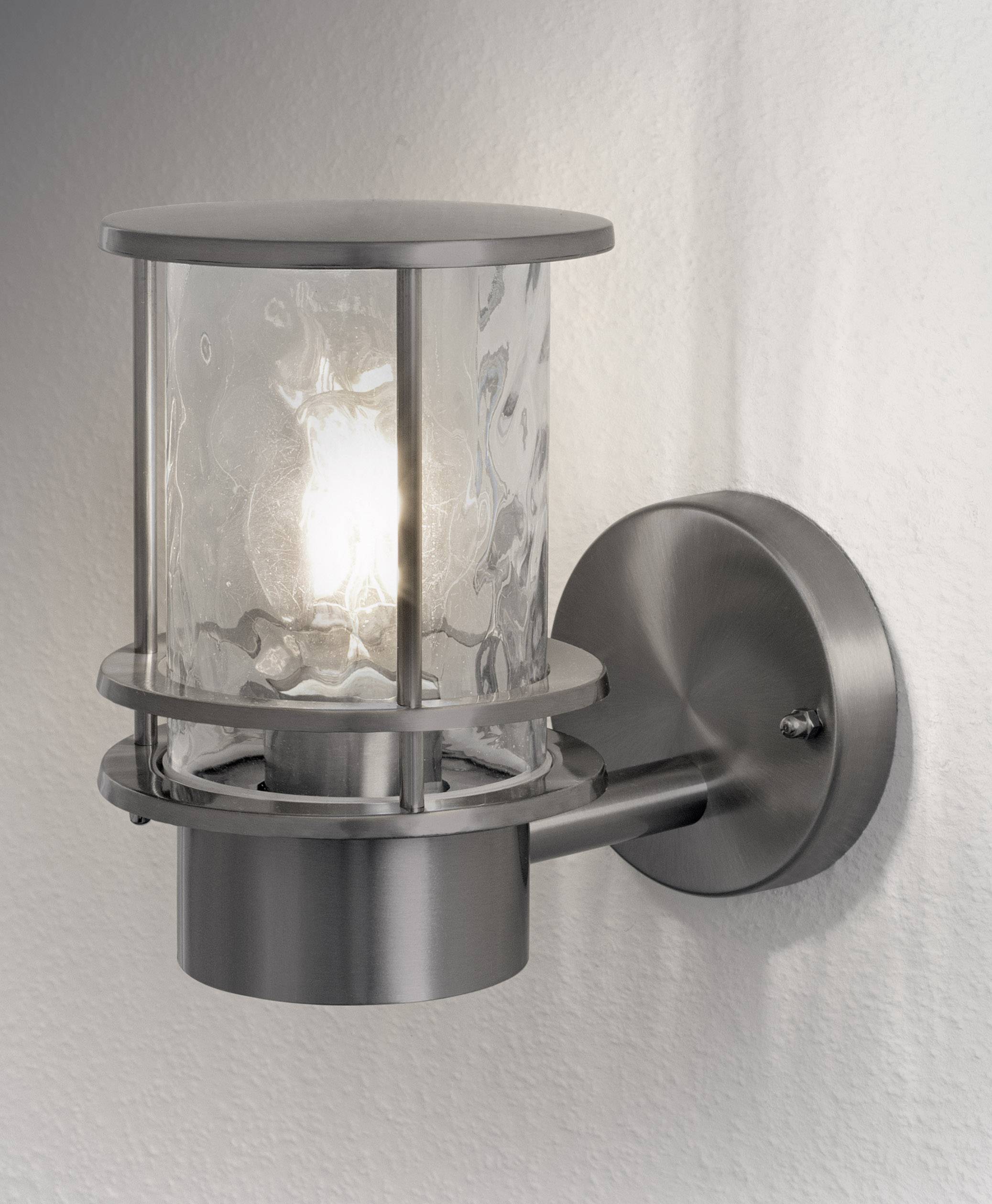 Applique murale moderne en acier inoxydable avec du verre transparent qui entoure une ampoule, éclairant un mur blanc.