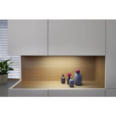Trois vases bleus avec des fleurs roses sont posés sur une étagère en bois dans un espace moderne et minimaliste aux armoires blanches.
