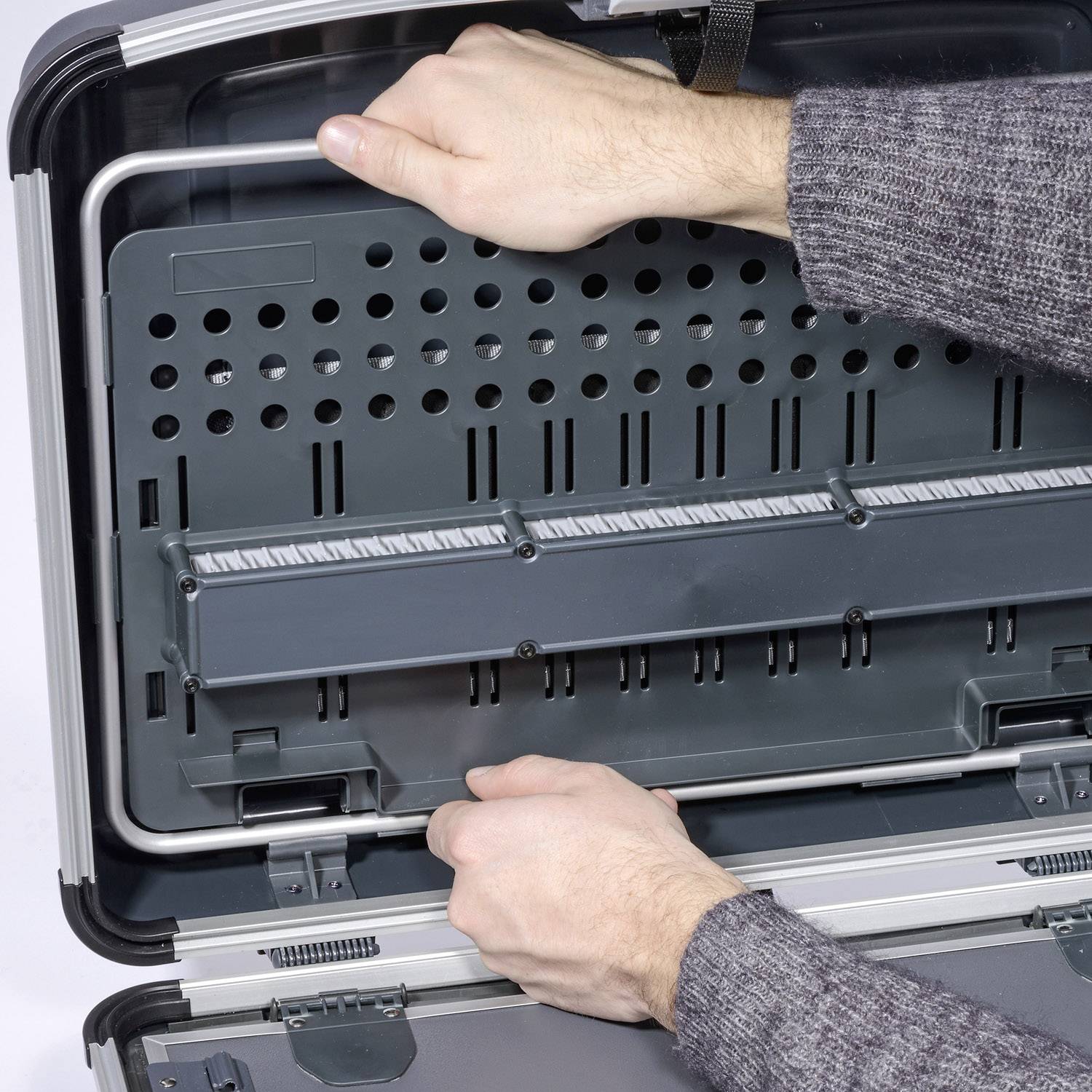 Une personne pointe du doigt un attaché-case ouvert et vide avec de nombreux compartiments.