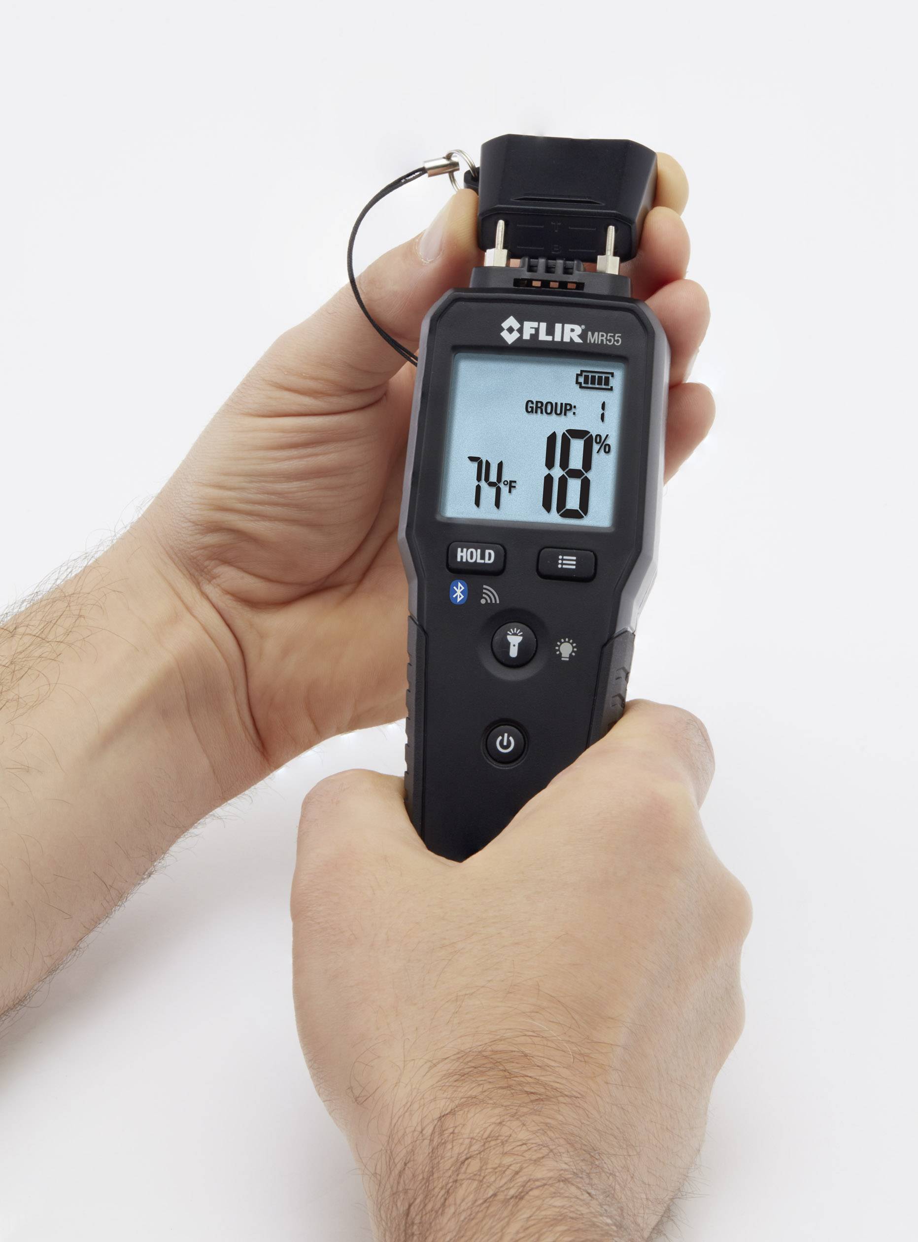 Une main tient un appareil de mesure numérique affichant '74' et '10%'. Il semble être utilisé pour mesurer l'humidité de l'air.