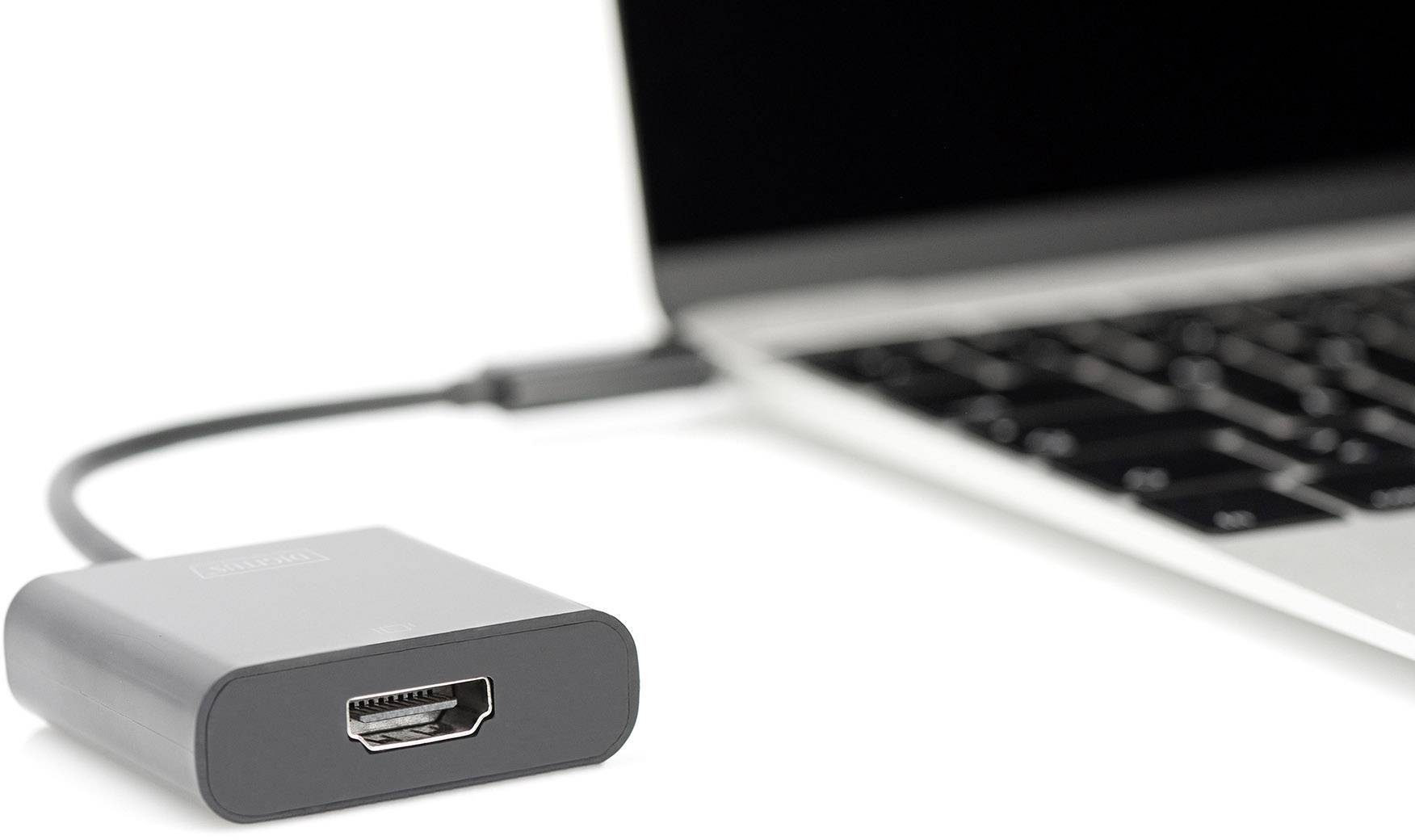 Un adaptateur HDMI noir est connecté à un ordinateur portable. L'ordinateur portable est partiellement visible, avec un focus sur le clavier.