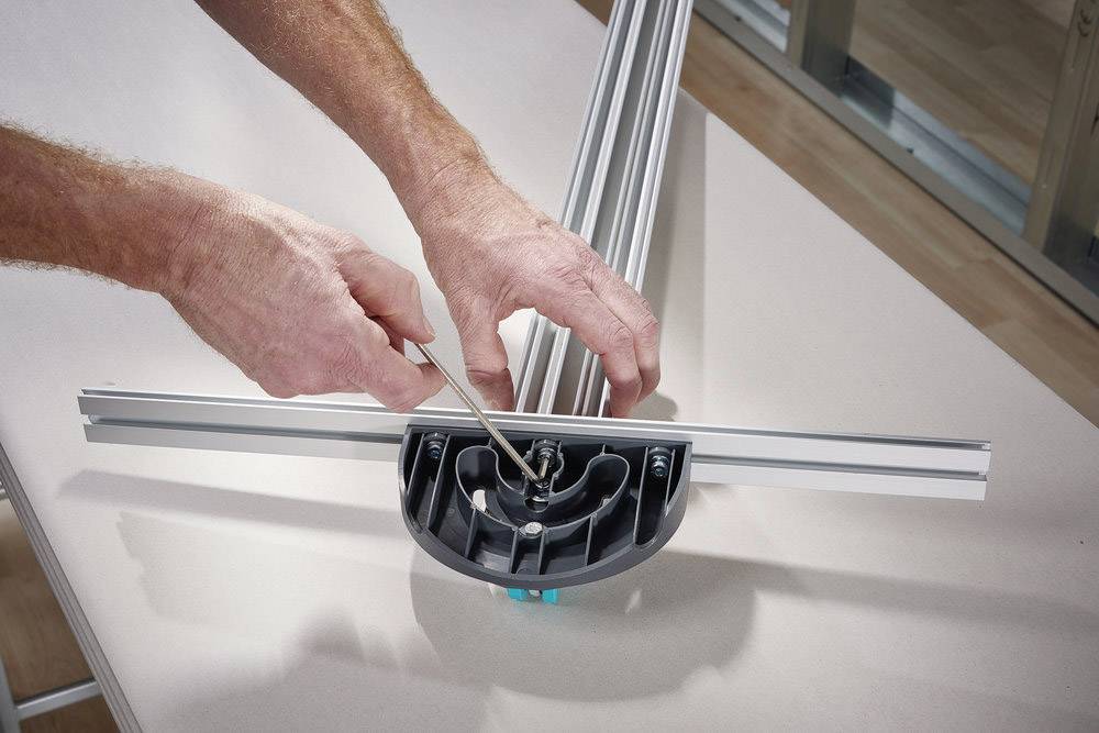 Une personne monte un châssis métallique à l'aide d'un tournevis. Le châssis est posé sur une table à l'intérieur d'un local.