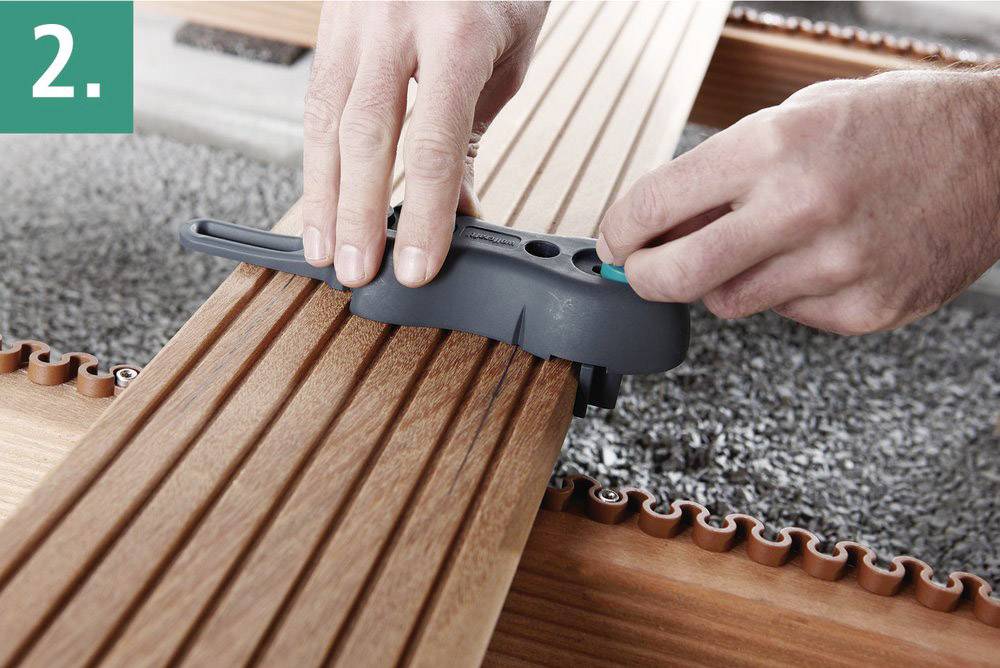 Une personne fixe une lame de terrasse en bois sur une structure support à l'aide d'un outil de montage. Étape 2.