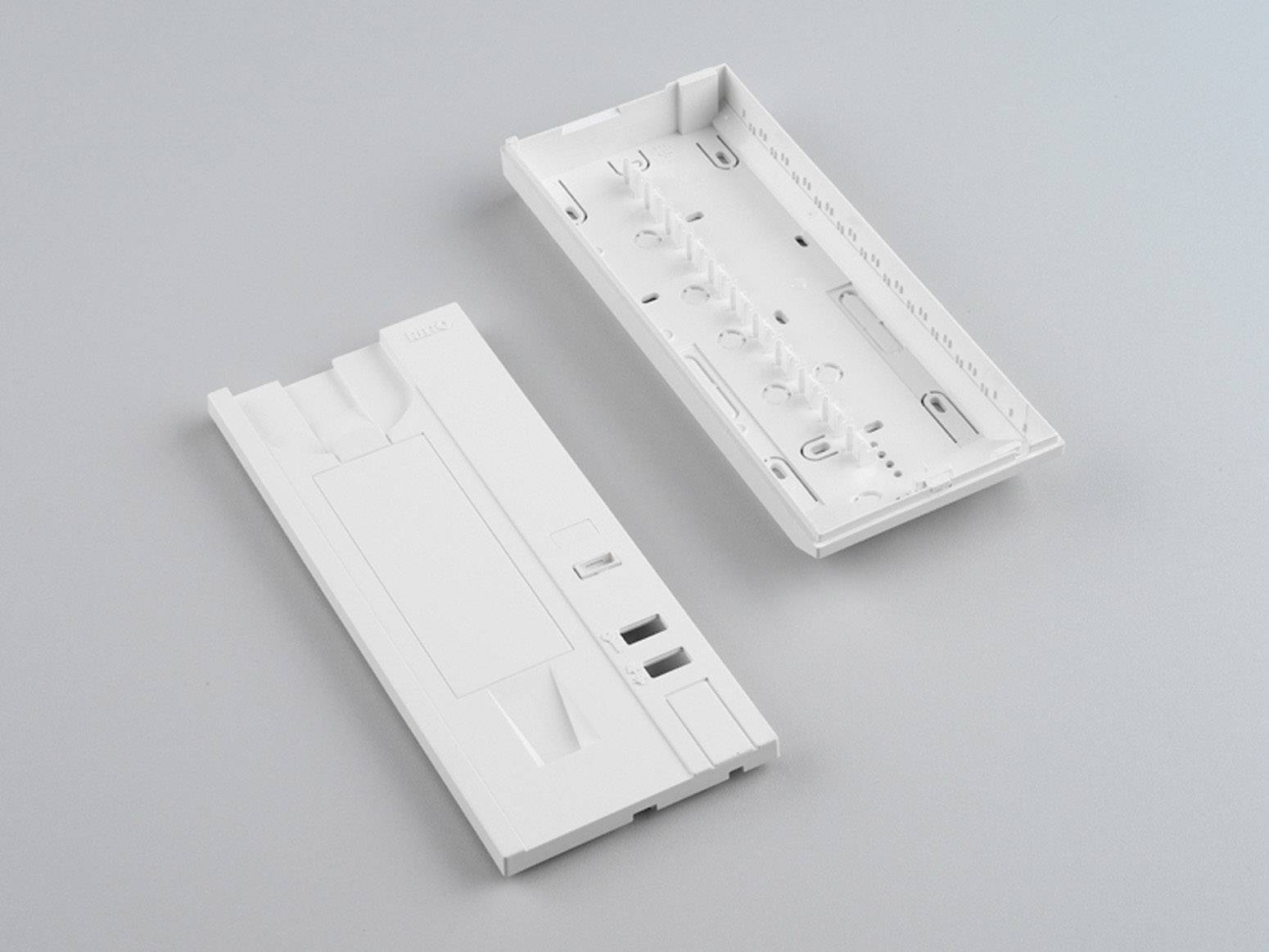 Deux couvercles en plastique blanc, l'un fermé et l'autre ouvert, montrent les faces intérieures ainsi que divers points de fixation et emplacements de connexion.