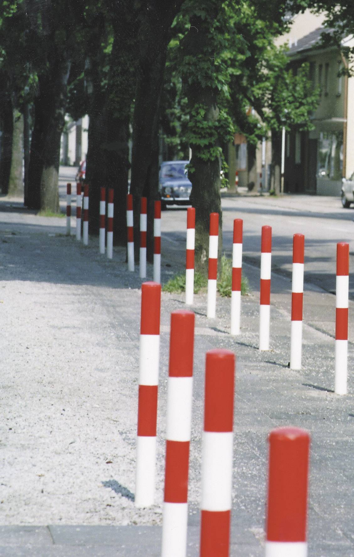 Des poteaux rouges et blancs le long d'un trottoir dans un environnement urbain, servant de barrière ou de délimitation de chemin.