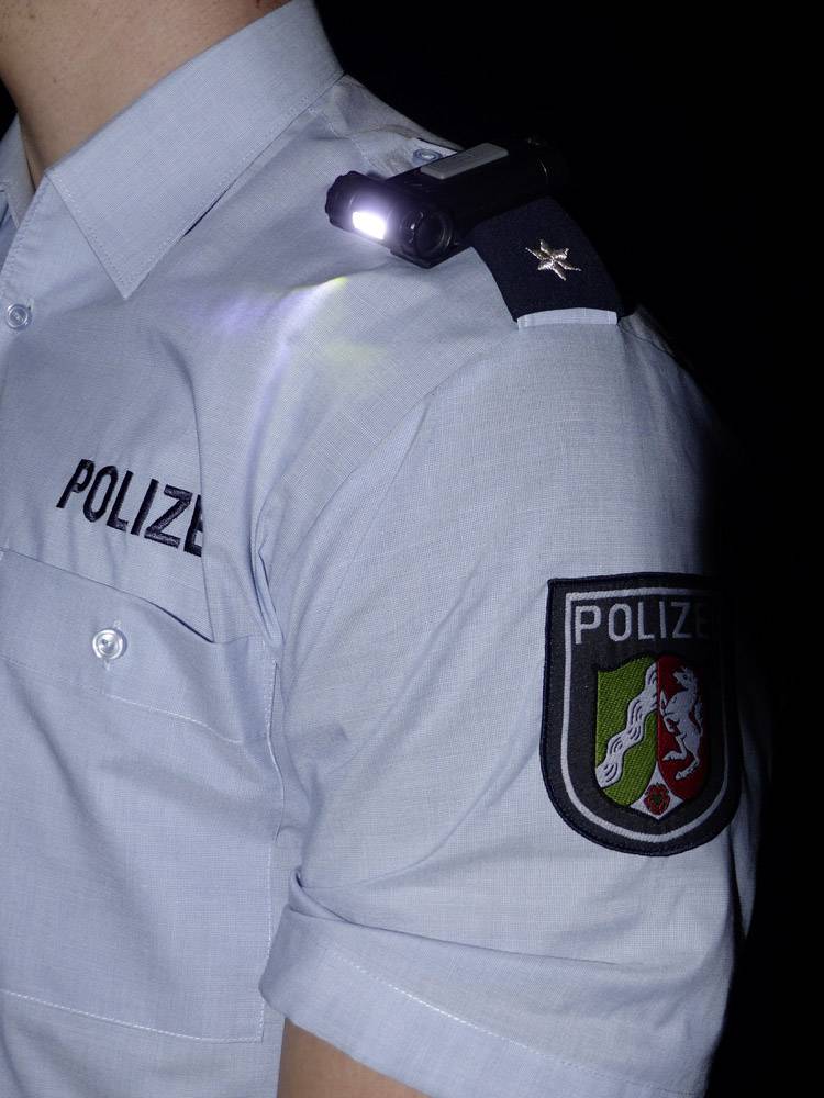 Chemise de policier uniforme avec une caméra de corps fixée sur l'épaule et un insigne portant l'inscription 'Police' sur un fond sombre.
