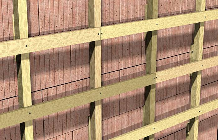 Des lattes de bois sont fixées uniformément sur un mur de briques.