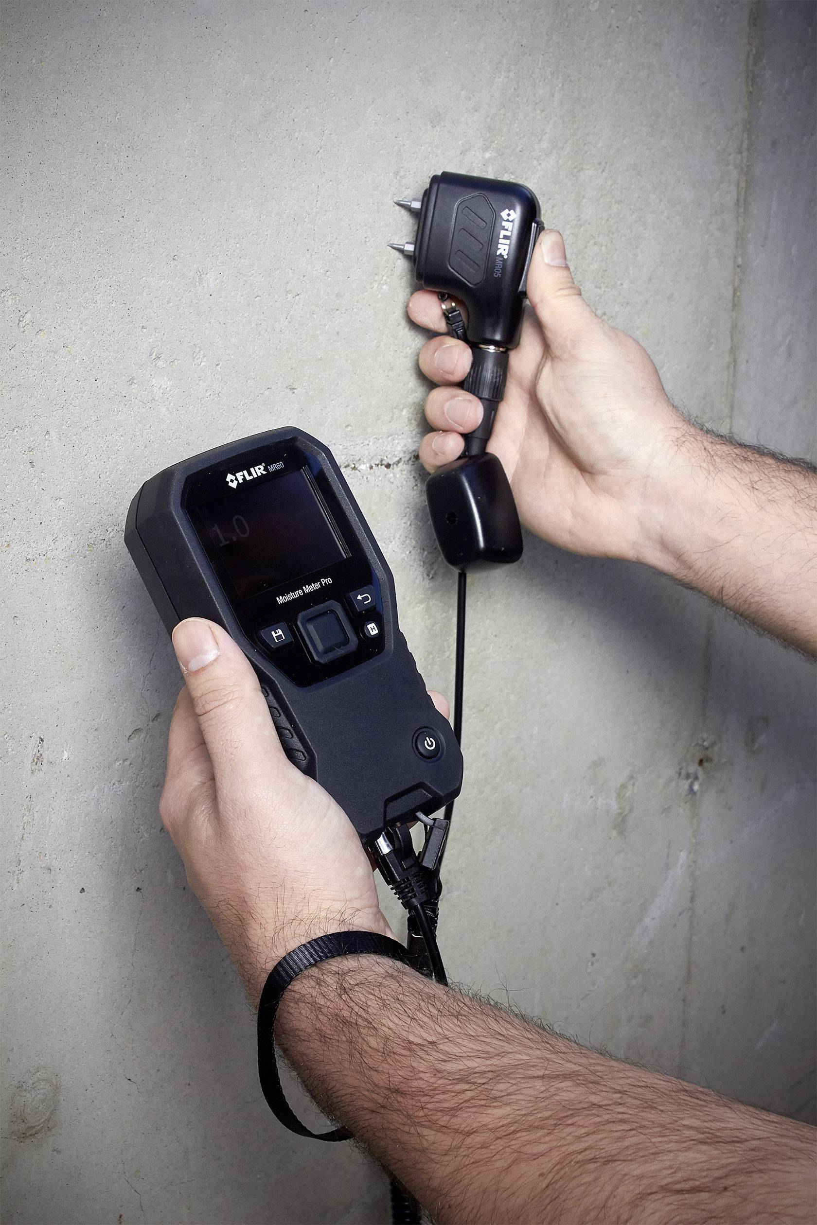 Un appareil portable est maintenu contre un mur en béton pour mesurer des valeurs sur l'écran.