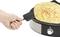 Une main retourne un crêpe doré-brun sur une crêpière électrique ronde avec régulateur de température.