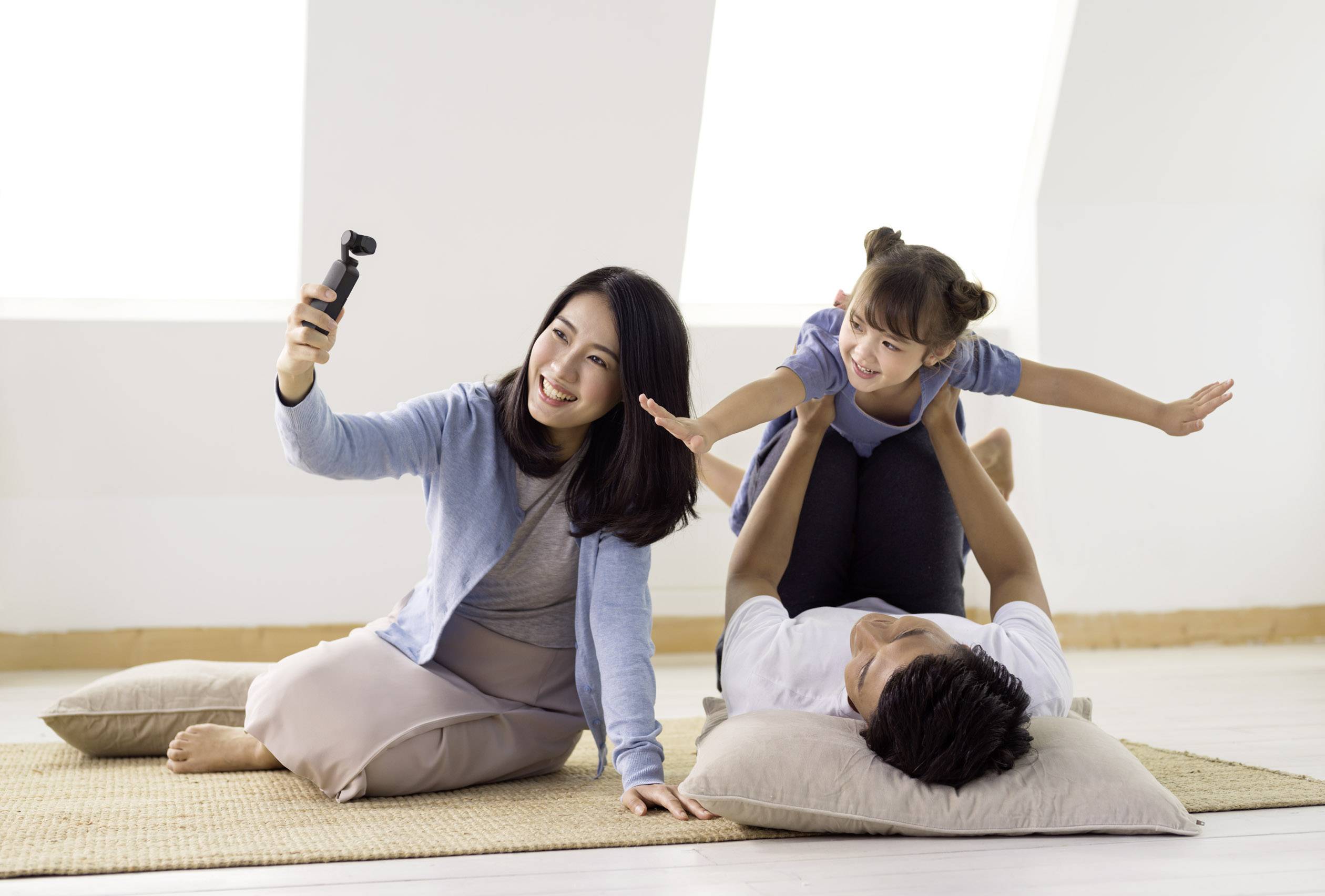 Une femme prend un selfie tandis qu'un homme est allongé sur le dos et fait équilibre avec un enfant riant sur ses jambes. Ils semblent joyeux.