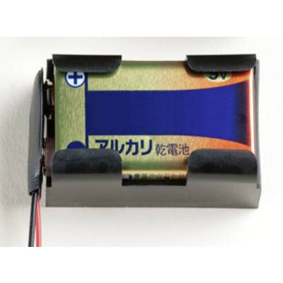 Une pile alcaline 9V dans un support de batterie noir, auquel sont fixés un câble rouge et un câble noir.