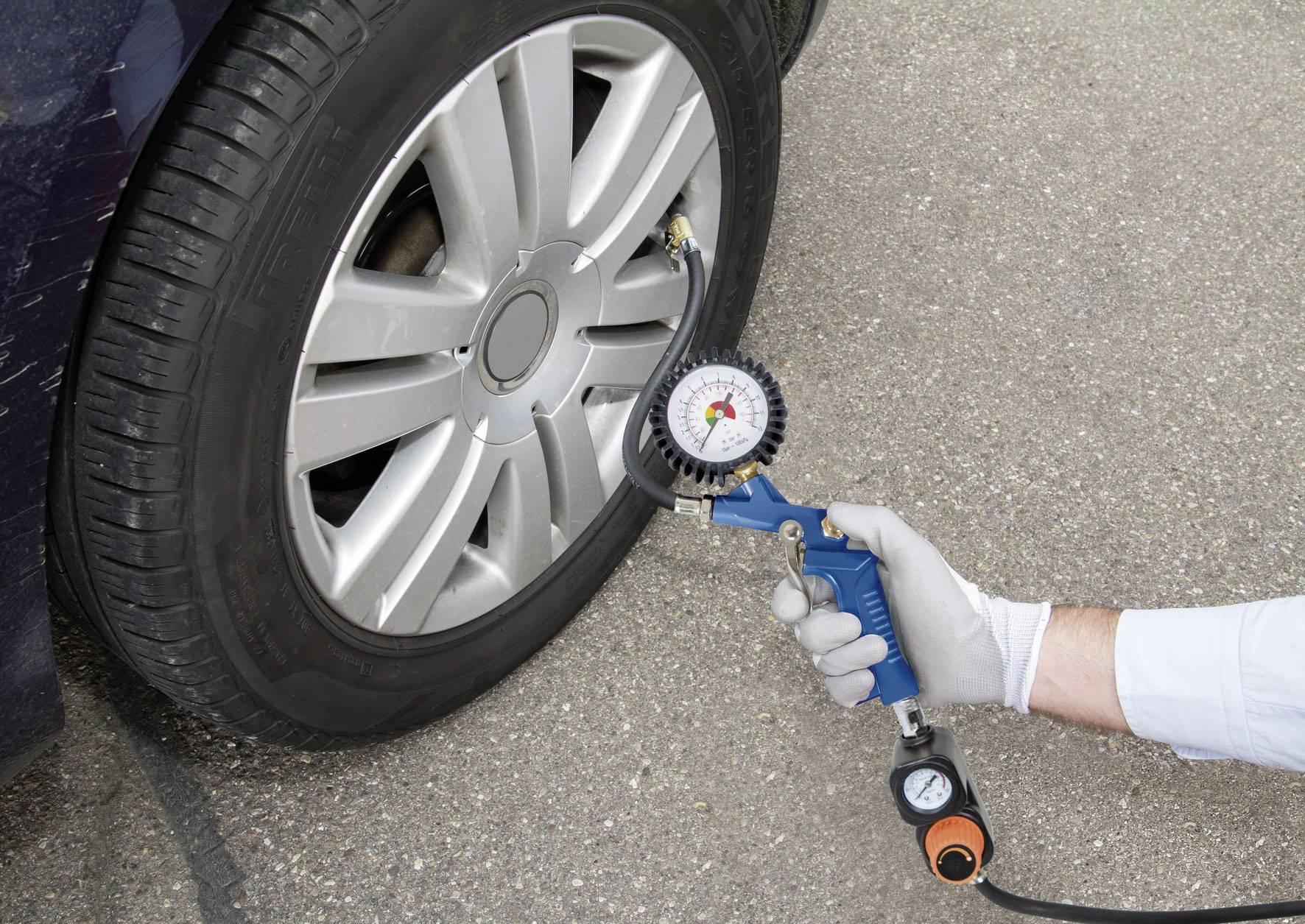 Une personne mesure la pression des pneus sur un pneu de voiture à l'aide d'un manomètre. Le pneu est posé sur un revêtement en asphalte.