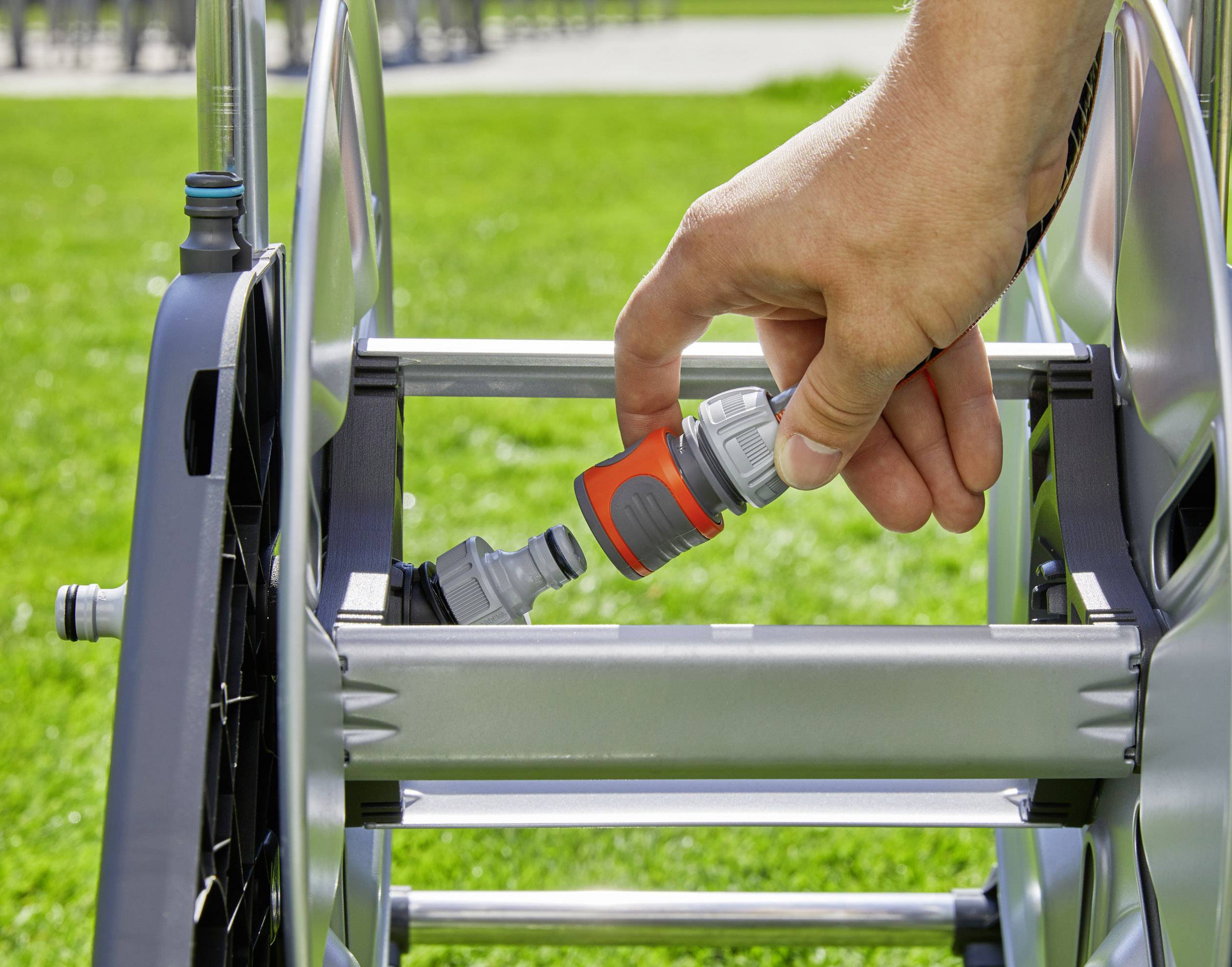 Une main branche un raccord de tuyau sur un chariot de tuyau dans un jardin. De l'herbe est visible en arrière-plan.